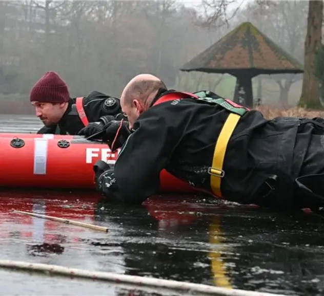 Zwei Männer mit Schlauchboot auf zugefrorenen See.