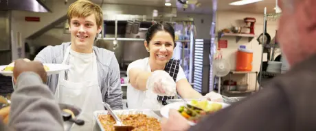 Ein Mann und eine Frau geben Essen in einer Kantine aus.