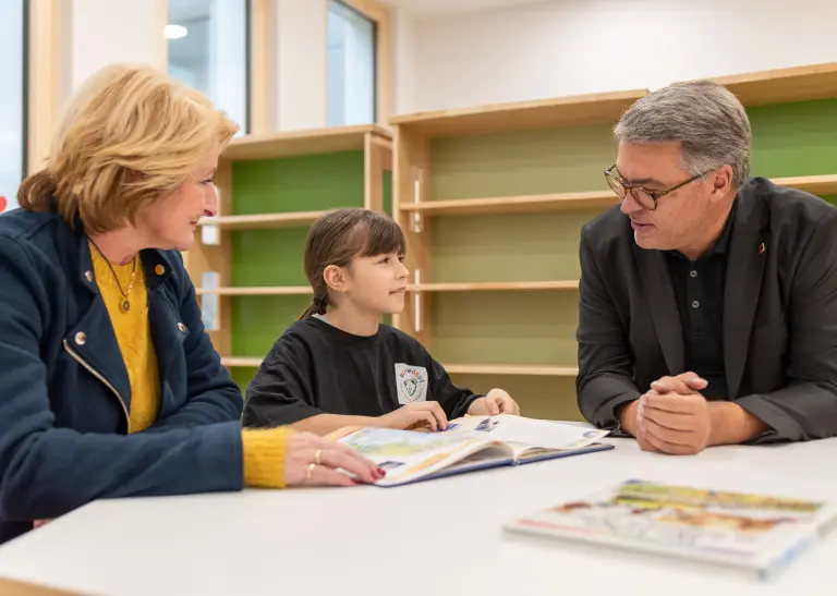 Oberbürgermeister Thomas Westphal sitz mit einem Kind und der Schulleiterin Anette König im Gespräch in der neuen Schule am Tisch.