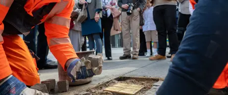 Im Vordergrund zwei Männer, die die Stolpersteine verlegen, im Hintergrund weitere Personen.