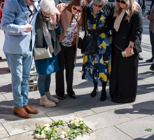 Mehrere Personen unterschiedlichen Alters stehen gebeugt über den Stolpersteinen