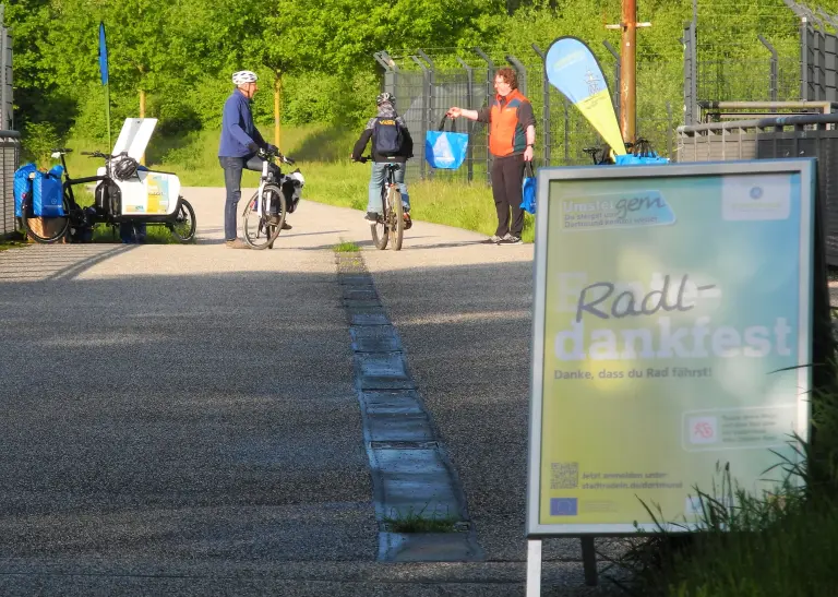 Im Vorderrund ein Aufsteller vom Projekt Stadtradeln. Im Hintergrund sind zwei Personen.