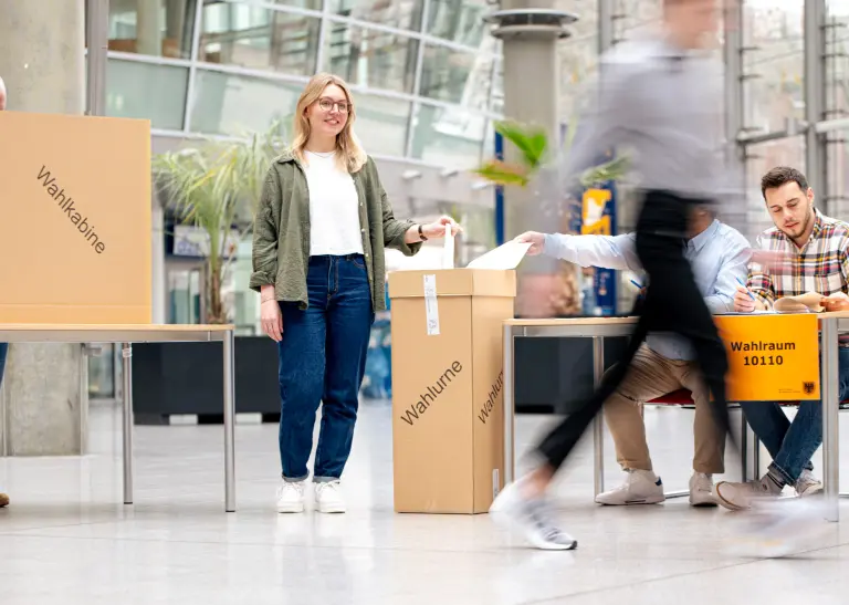 Menschen helfen bei einer Wahl mit, eine junge Dame ist im Vordergrund zu sehen.