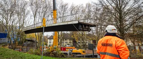 Eine Brücke über die B1 wird mit einem Kran angehoben, im Vordergrund steht ein Arbeiter