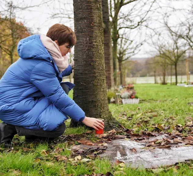 Frau zündet Kerze an Obstbaumgrab an.