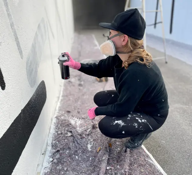 Eine junge Frau sprüht etwas an eine Wand.