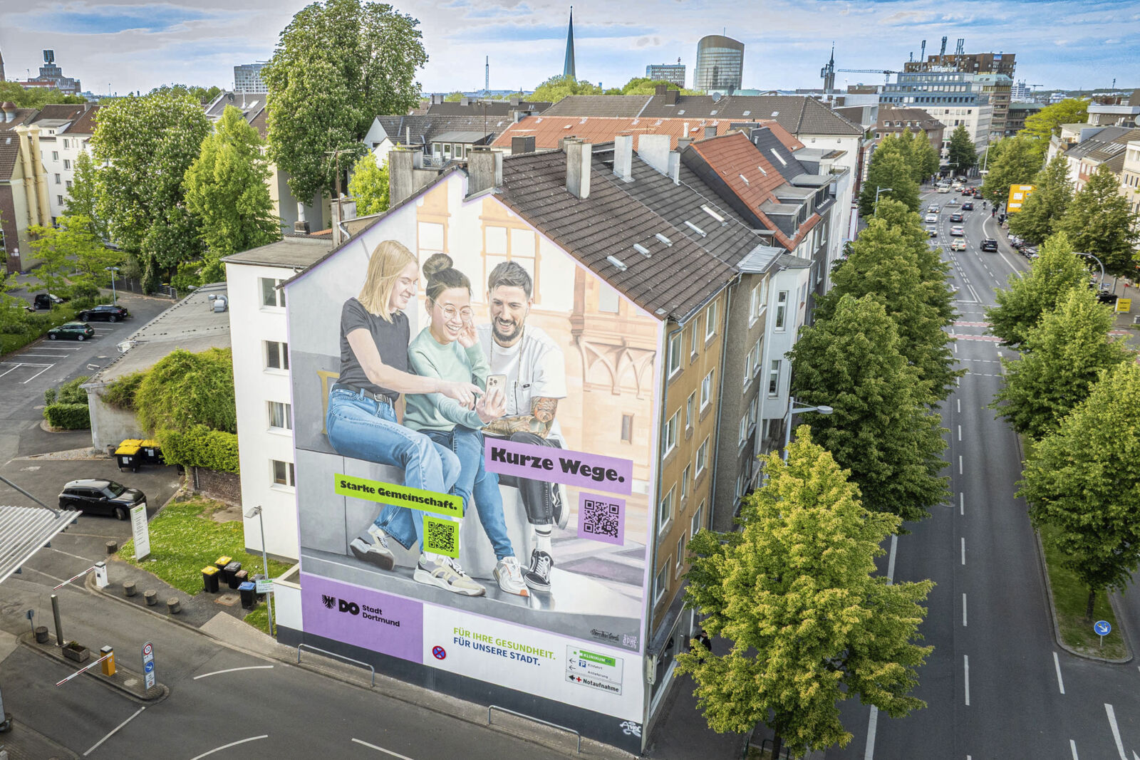 Ein großes Bild an einer Hauswand an der Hohen Straße zeigt drei Personen, die auf ein Handy schauen und lächeln.