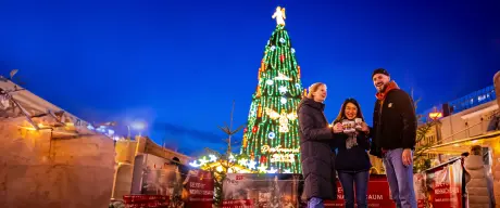 Personen stoßen vor Weihnachtsbaum mit Tassen an