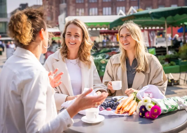 Steffi Strecker mit zwei jungen Frauen an einem Tisch auf dem Wochenmarkt