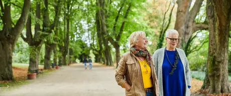 Zwei Seniorinnen spazieren lachend durch den Rombergpark.