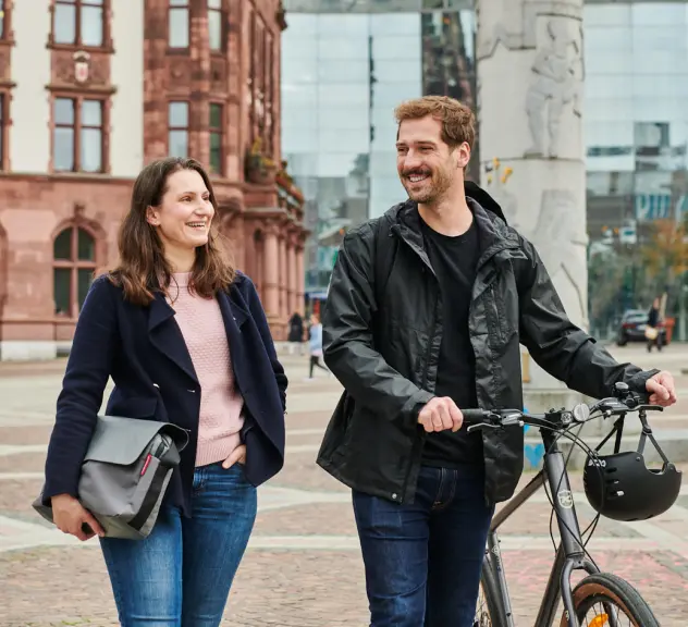 Zwei Personen laufen mit Tasche und Fahrrad über den Friedensplatz