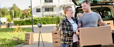 Zwei Personen mit einem Umzugskarton auf dem Weg vom Auto zu ihrer neuen Wohnung