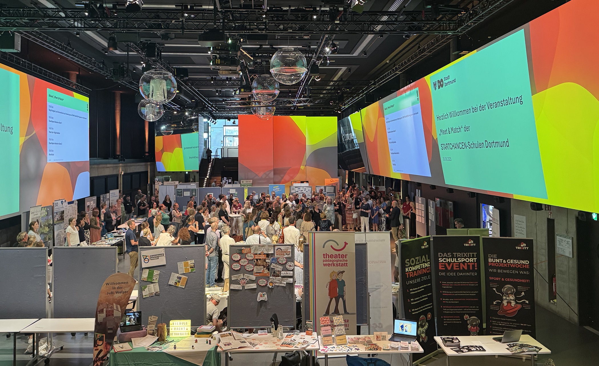 Blick in eine große Halle mit vielen Menschen und Ständen.