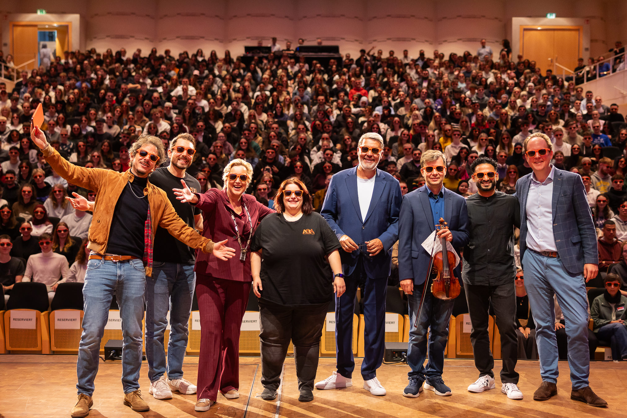 Im Konzerthaus Dortmund begrüßte FH-Rektorin Prof. Dr. Tamara Appel (3.v.l.) gemeinsam mit Oberbürgermeister Thomas Westphal (4.v.r.) und Vertreter*innen des AStA die neuen Erstsemester. Die Moderation übernahm Rainer Holl (l.). Die Dortmunder Philharmoniker mit ihrem Generalmusikdirektor Jordan de Souza und Konzertmeister Alexander Prushinskiy (2.u.3.v.r.) empfingen die Erstis musikalisch. Konzerthaus-Intendant Dr. Raphael von Hoensbroech (r.) verloste spontan Konzerttickets an die neuen Studierenden.
