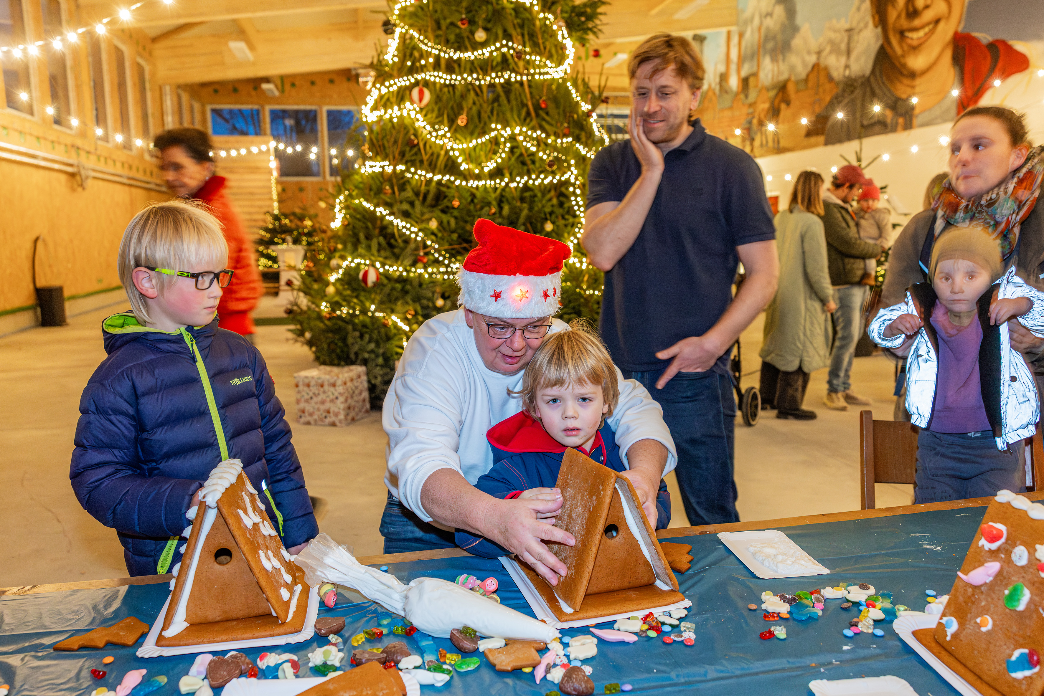 Erwachsene backen mit Kindern ein Lebkuchenhaus.