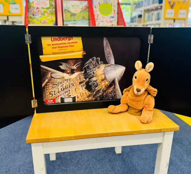 Ein Bild zur Geschichte sowie ein Känguru-Stofftier auf einem Tisch in der Bibliothek