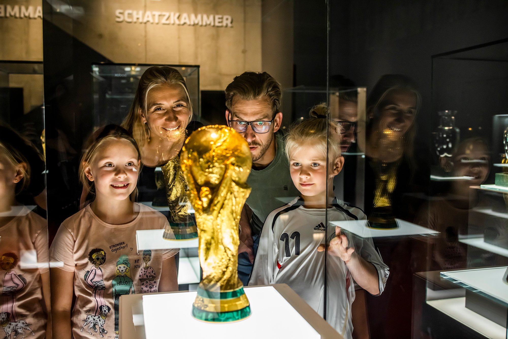 Familie schaut einen Pokal hinter einer Glasscheibe an.