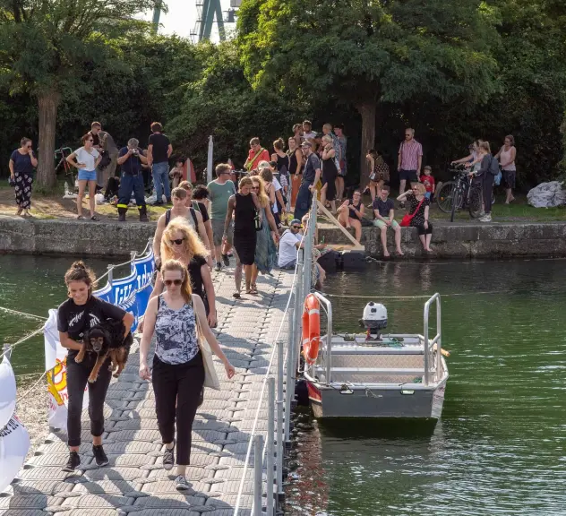 Zahlreiche Menschen am Dortmunder Hafen beim Hafenspaziergang. Im Vordergrund gehen einige Personen über die Pontonbrücke, eine schwimmende Brücke auf dem Wasser, die für den Hafenspaziergang eingerichtet wurde.