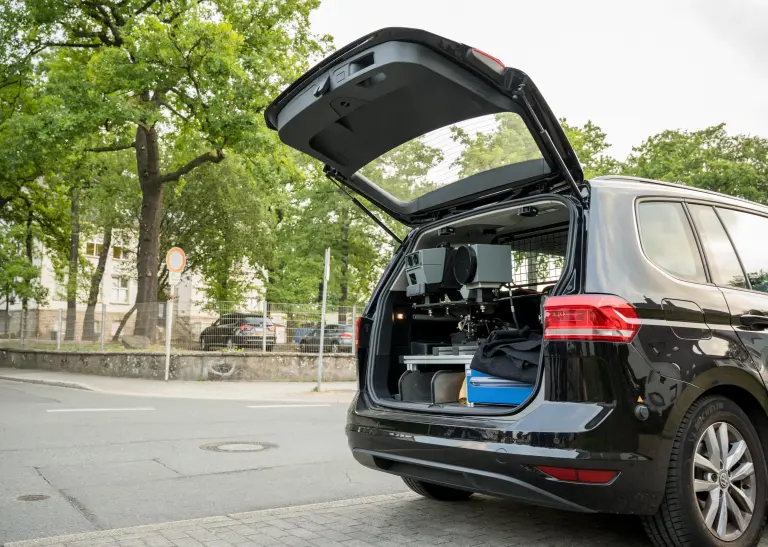 Ein Auto mit geöffnetem Kofferaum, im Kofferaum steht eine mobile Blitzeranlage, die nach außen gerichtet ist. Das Auto steht am Straßenrand an einer Kreuzung, im Hintergrund sind Bäume.