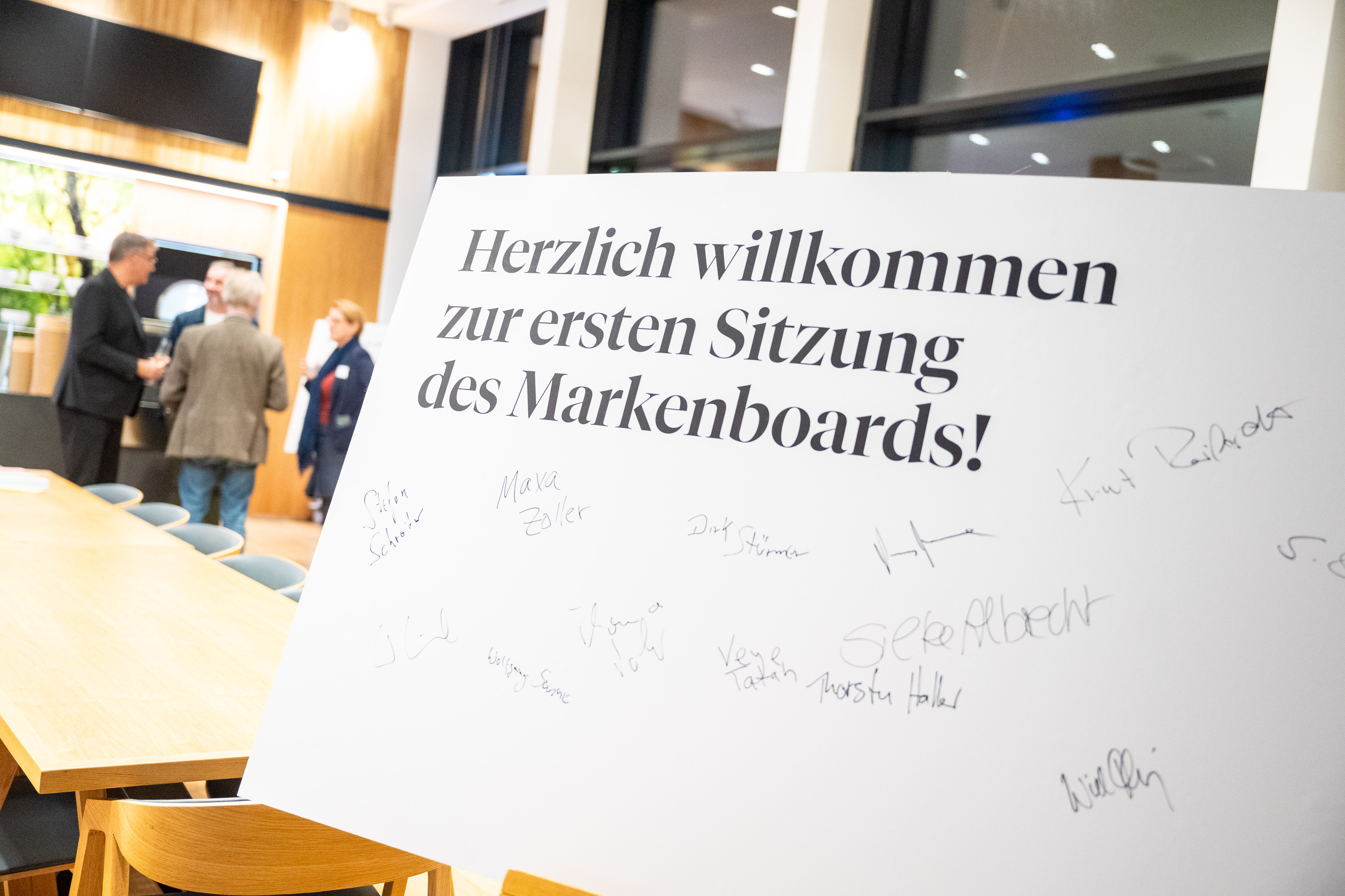 Ein weißer Aufsteller mit verschiedenen Unterschriften. Text: "Herzlich willkommen zur ersten Sitzung des Markenboards!"