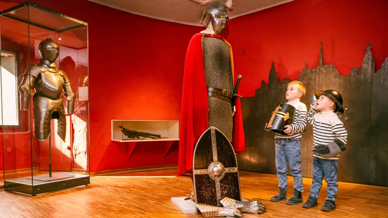 zwei Kinder bestaunen eine Ritterrüstung im Adlerturm