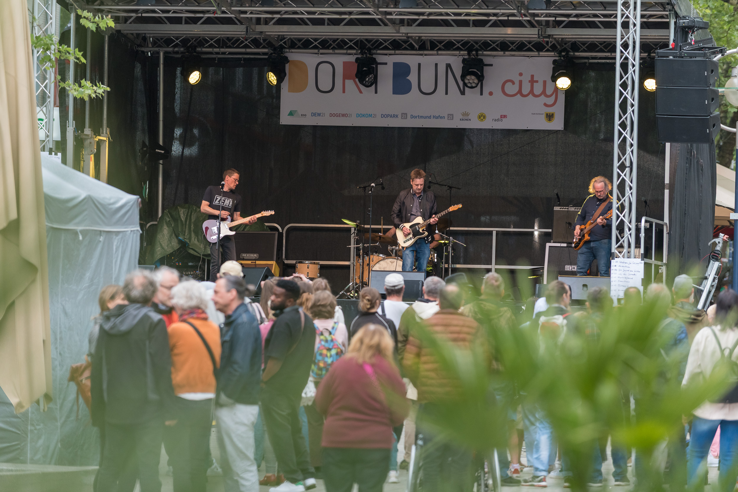 Eine Band spielt auf einer Bühne, im Vordergrund eine Menschenmenge.
