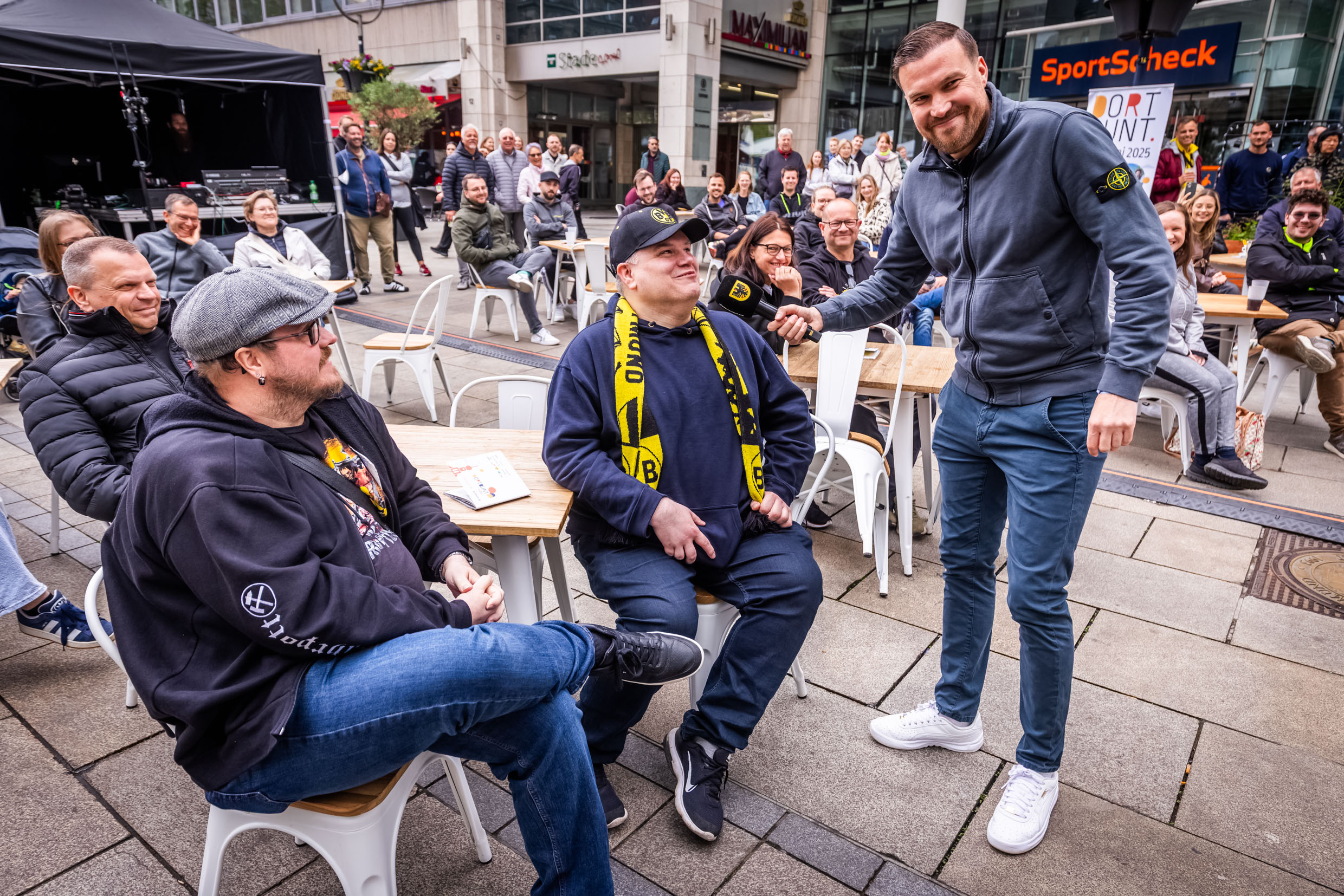 Kevin Großkreutz steht mit einem Mikrofon neben einem Mann und spricht mit ihm.