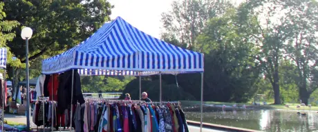 Stände mit Kleidung und Büchern auf dem Trödelmarkt im Westfalenpark Dortmund bei sonnigem Wetter mit dem Florian-Turm im Hintergrund.