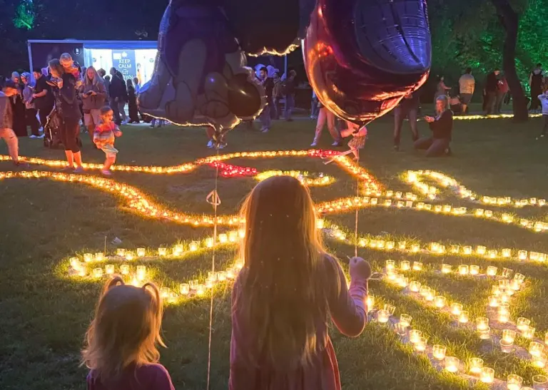 Kinder beobachten beleuchtete Wegführung beim Lichterfest im Westfalenpark, mit Luftballons und Kerzenlicht in der Dämmerung