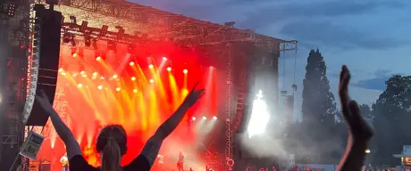 Publikum genießt ein Konzert bei Abenddämmerung im Westfalenpark mit erhobenen Händen und Bühnenbeleuchtung im Hintergrund.