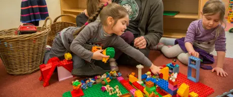 Ein junger Mann spielt in einer Kita mit mehreren Kindern