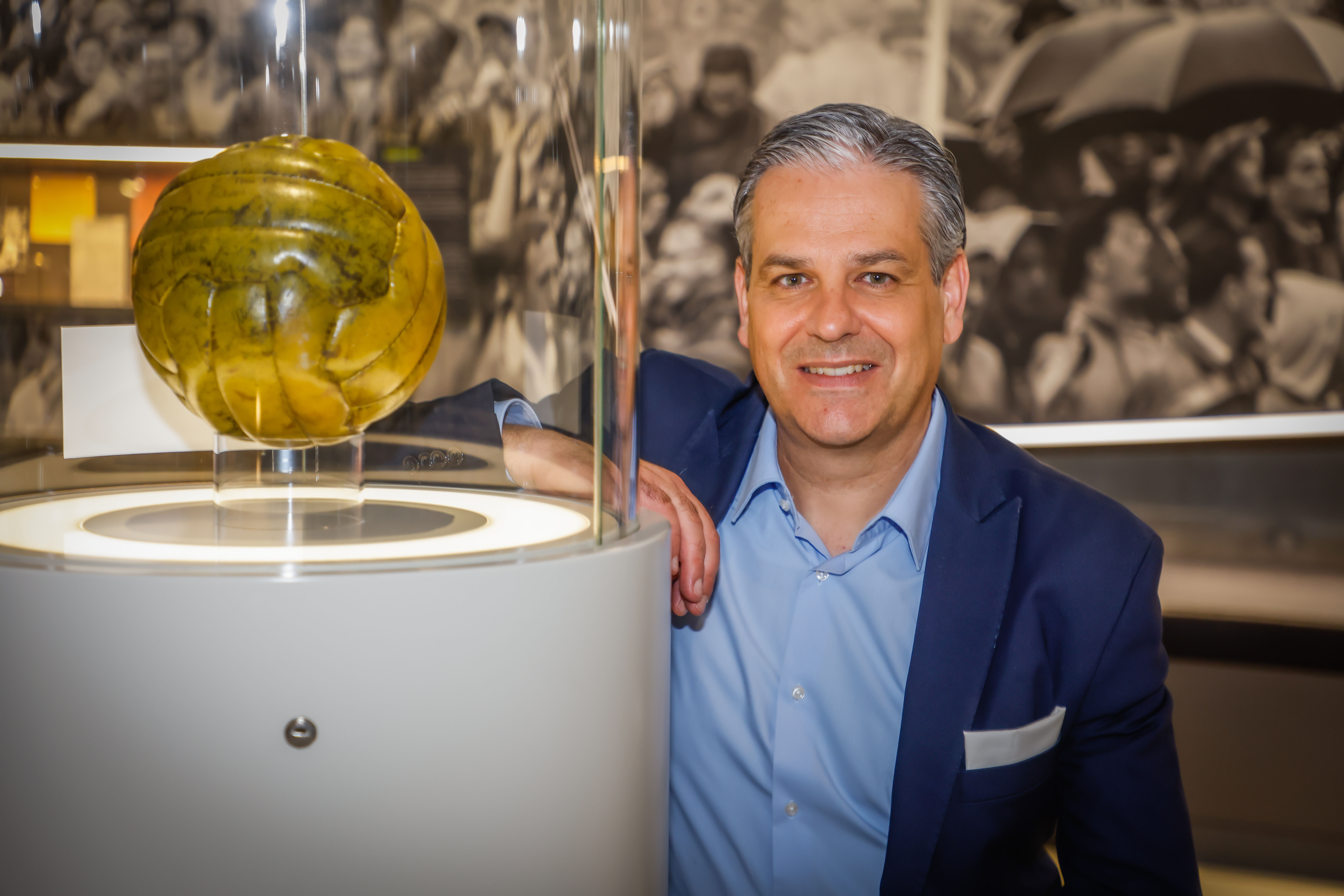 Foto eines Mannes neben einer Vitrine mit einem goldenen Fußball