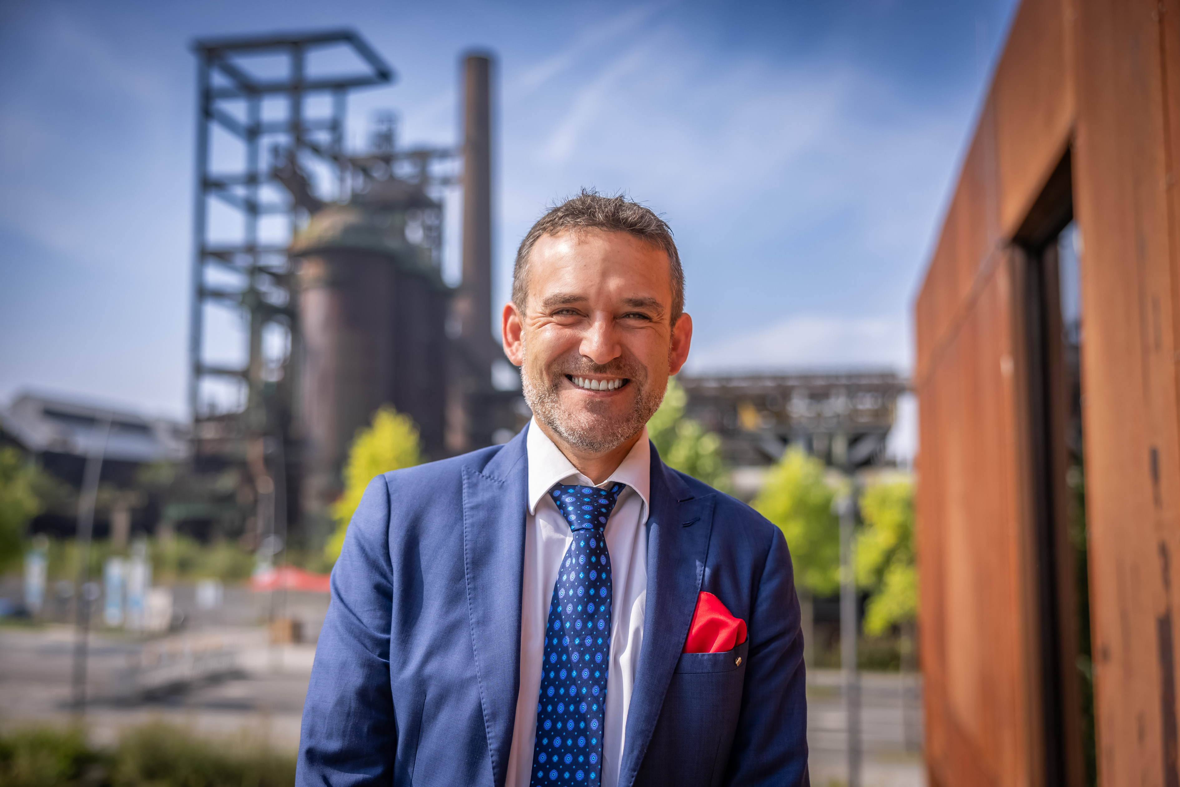Foto eines Mannes, im Hintergrund eine industrielle Anlage.