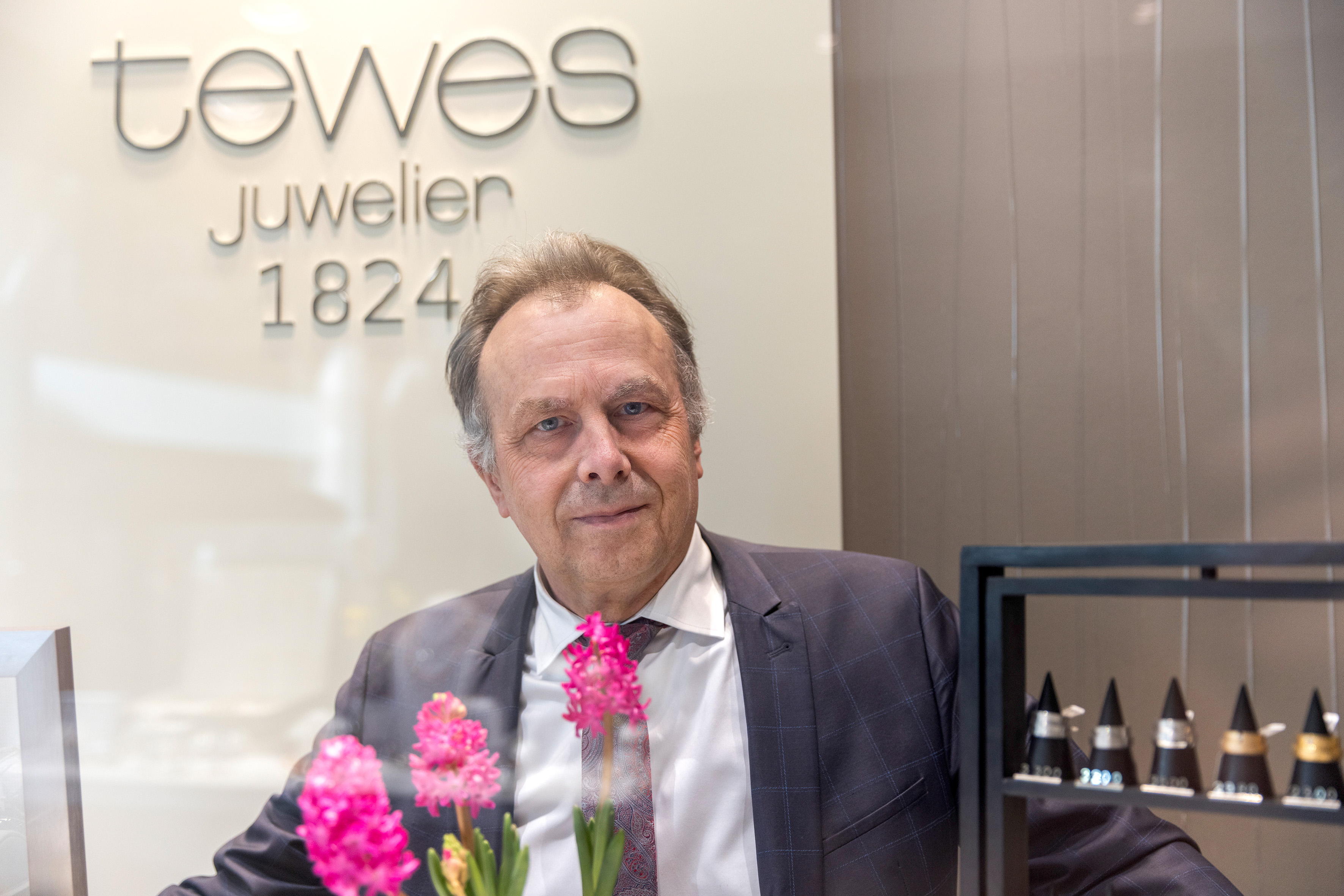 Foto eines Mannes, im Vordergrund Blumen, im Hintergrund der Schriftzug Juwelier Tewes