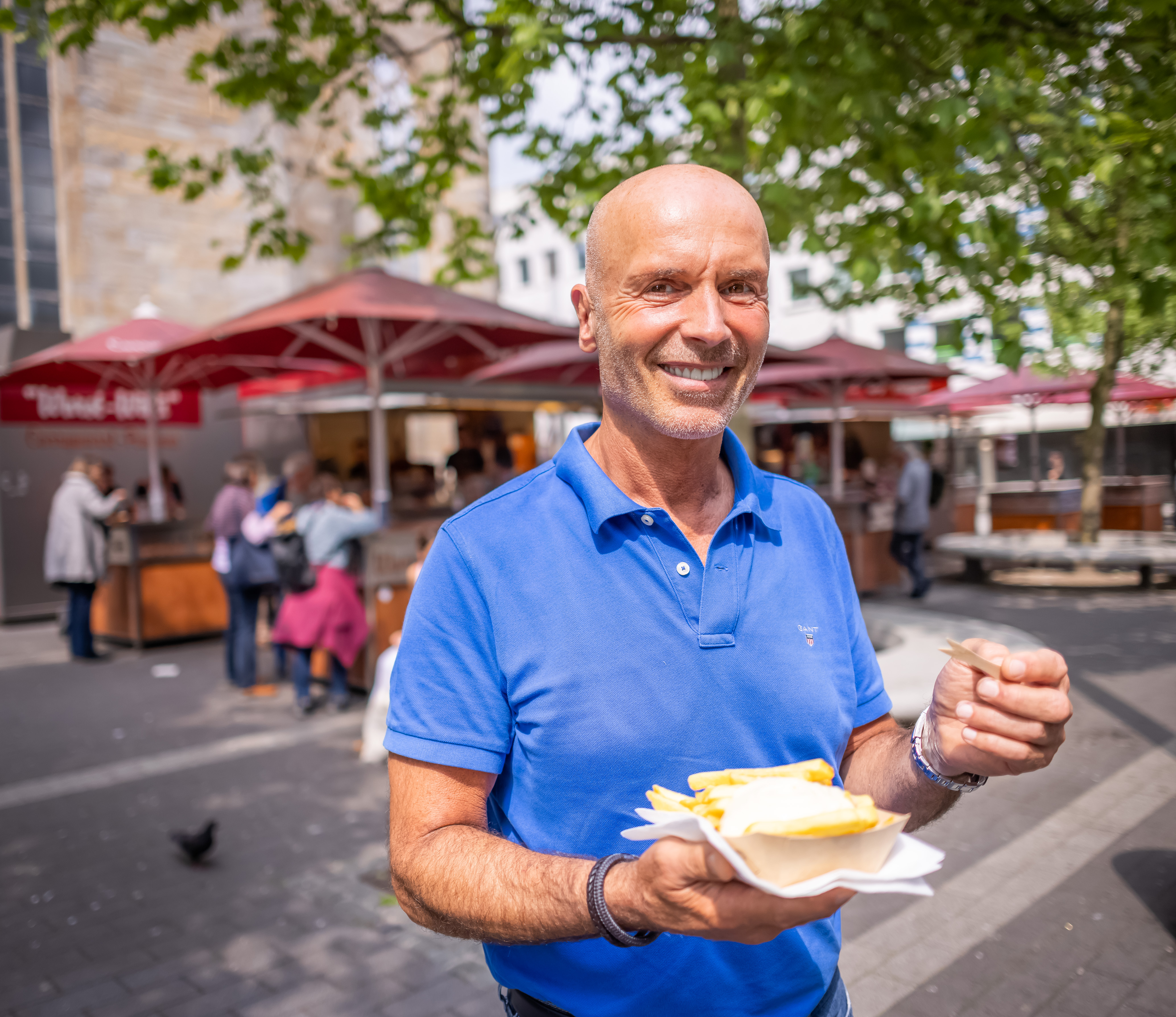 Foto eines Mannes mit einer Schale Pommes-Frites in der Hand, im Hintergrund ein Imbisswagen.