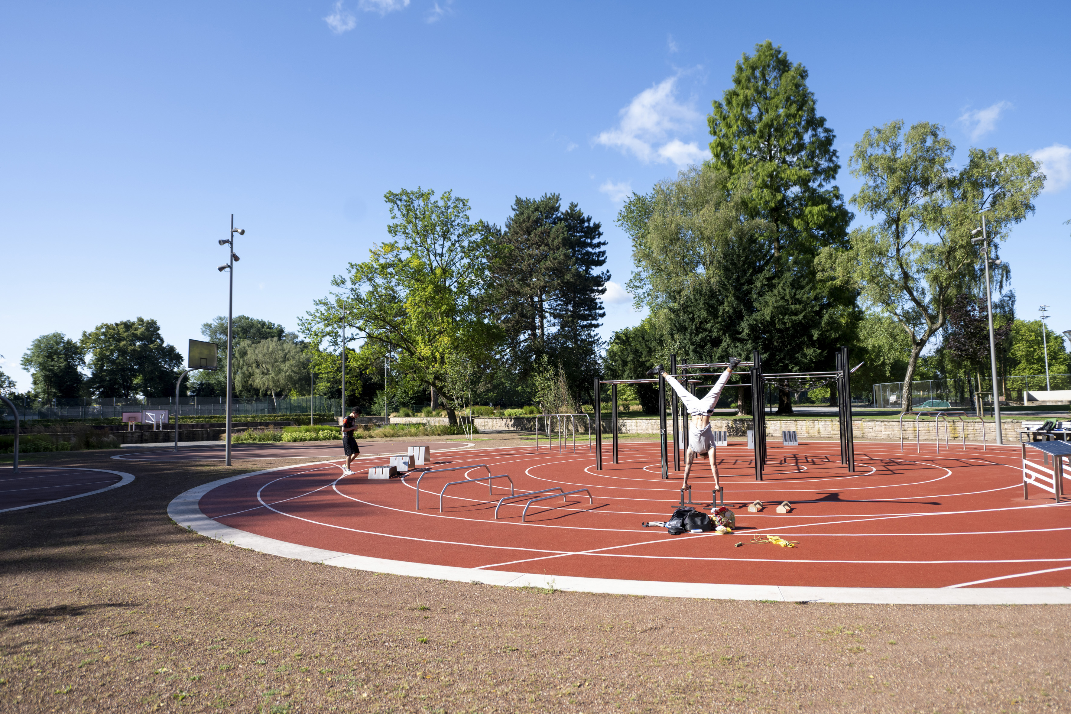 Ein Mann macht auf einer Calisthenics-Anlage mit rotem Untergrund und umgeben von Bäumen einen Handstand.