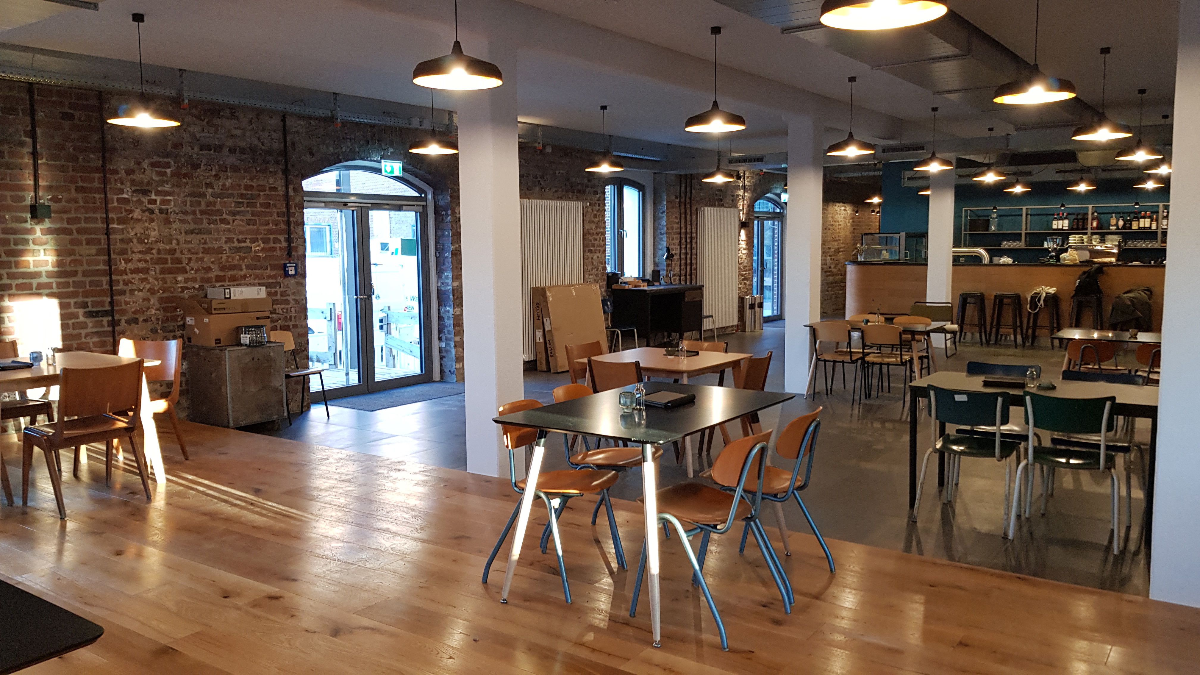 Gastraum mit Stühlen, Tischen, Bar und Leuchten und sichtbarem Backsteinwerk