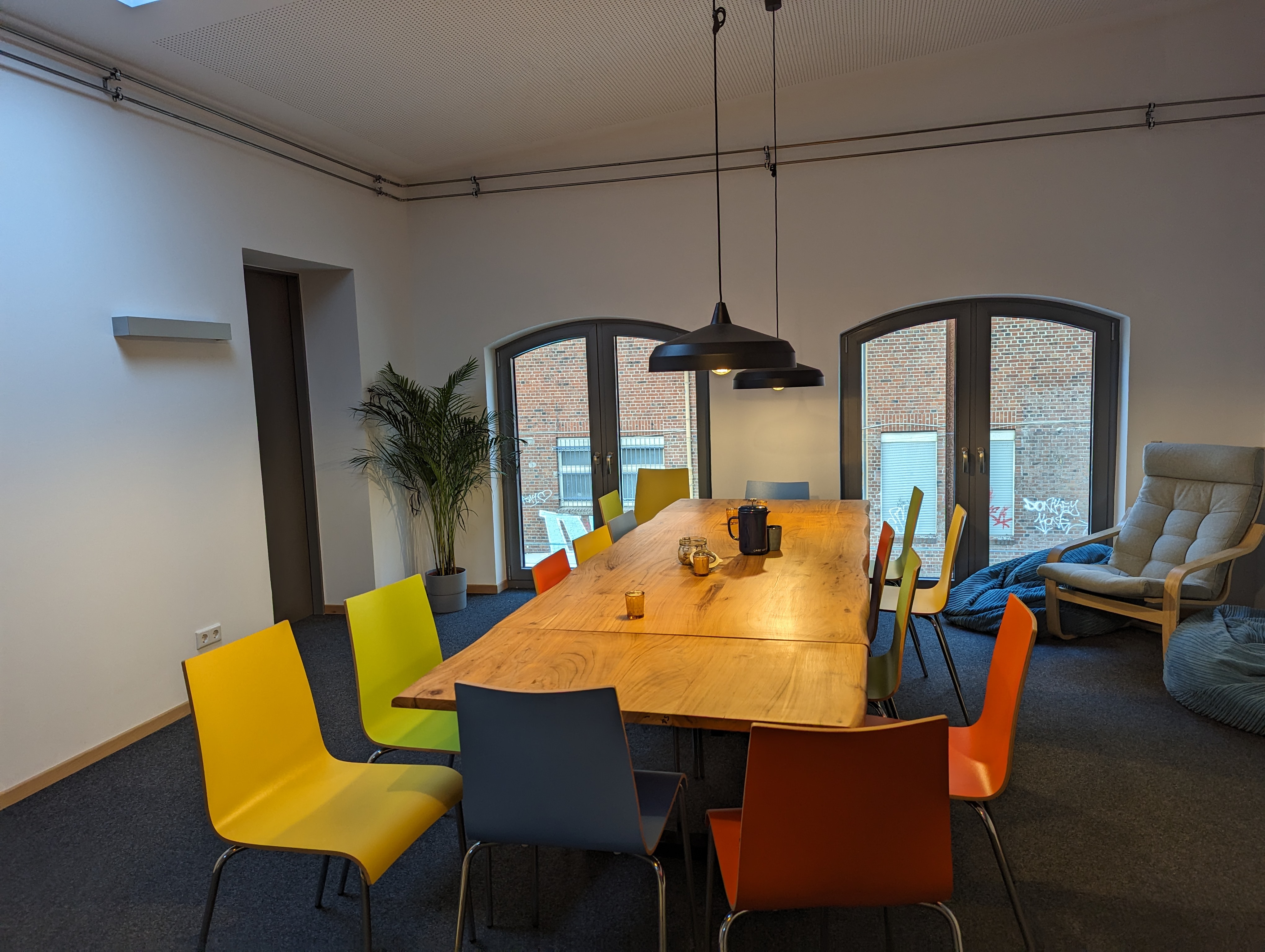 Raum mit bunten Stühlen um einen großen Holztisch.