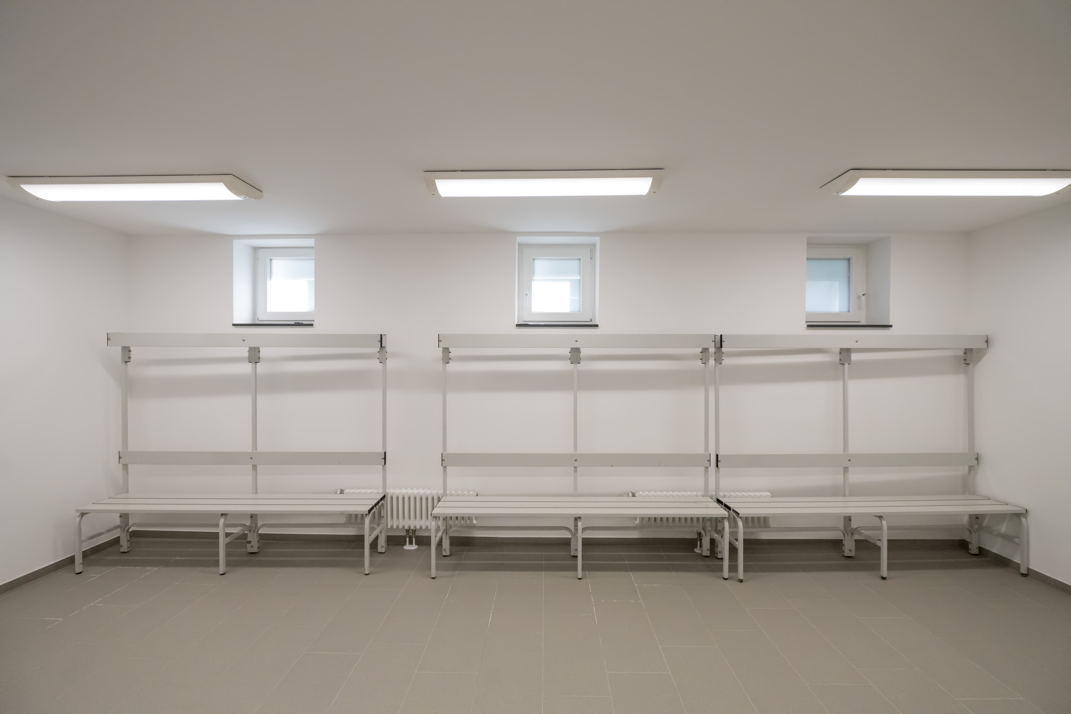 Bänke mit Garderobenhaken in einer hellen Umkleidekabine mit schmalen Oberlichtern. 