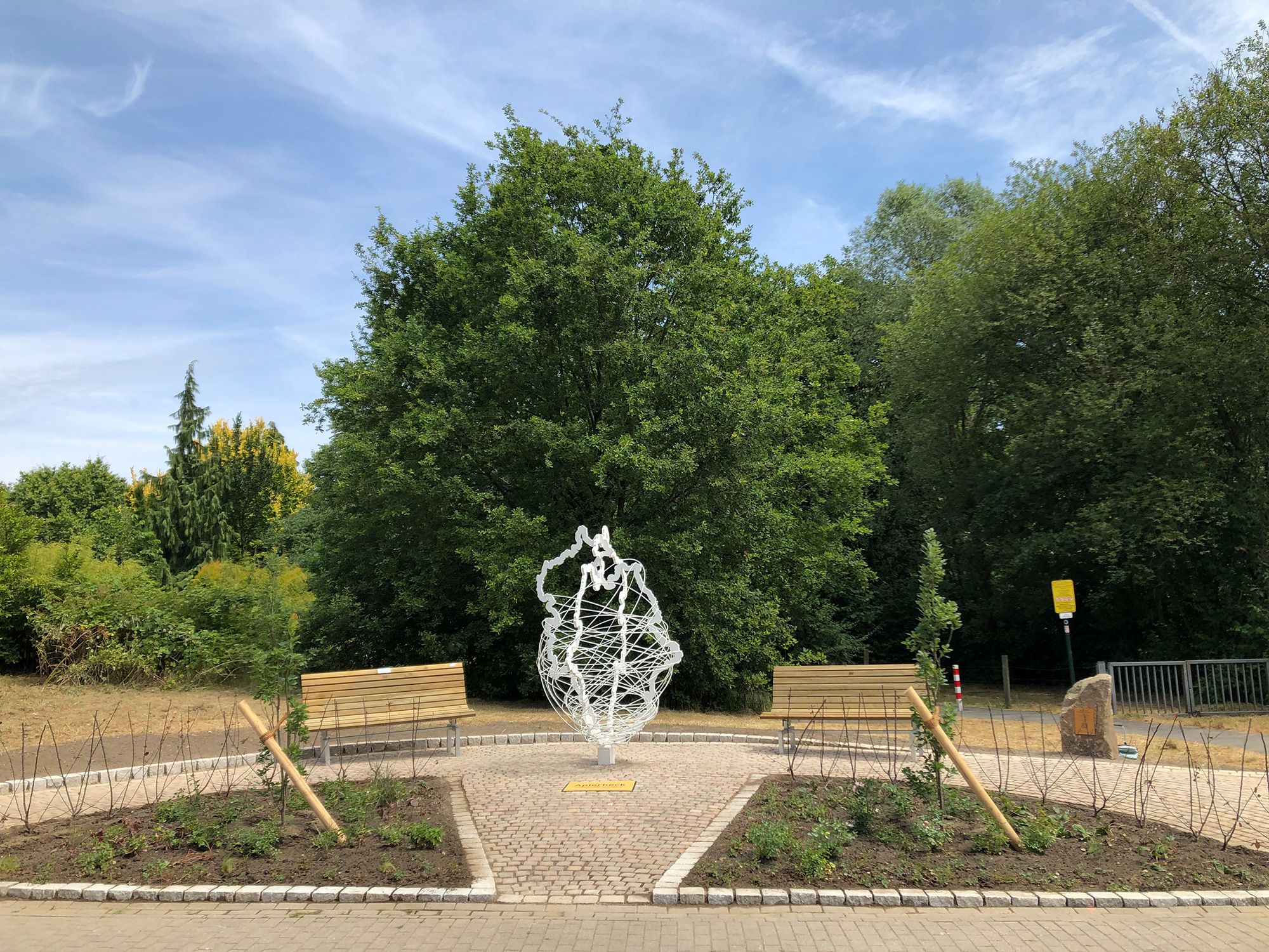 Ein silbernes Kunstwerk mit zwei Bänken in einer parkähnlichen Umgebung