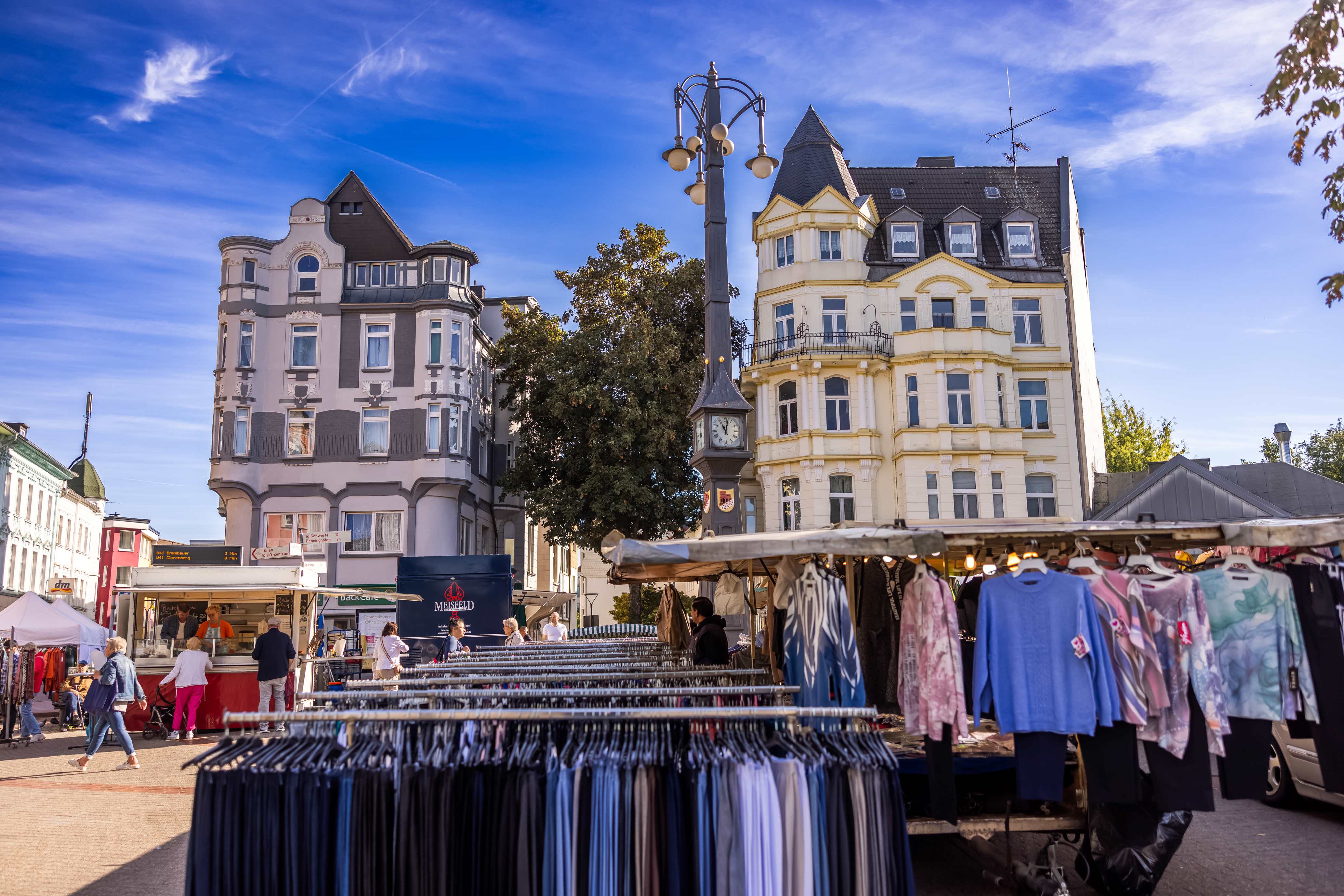 Ein Marktplatz mit Häuserfassaden im Hintergrund, im Vordergrund Marktstände.