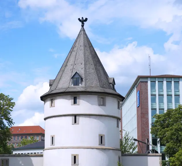 Zu sehen ist der runde weiße Adlerturm mit seinem grauen spitzen Dach und einem Adler auf der Turmspitze.