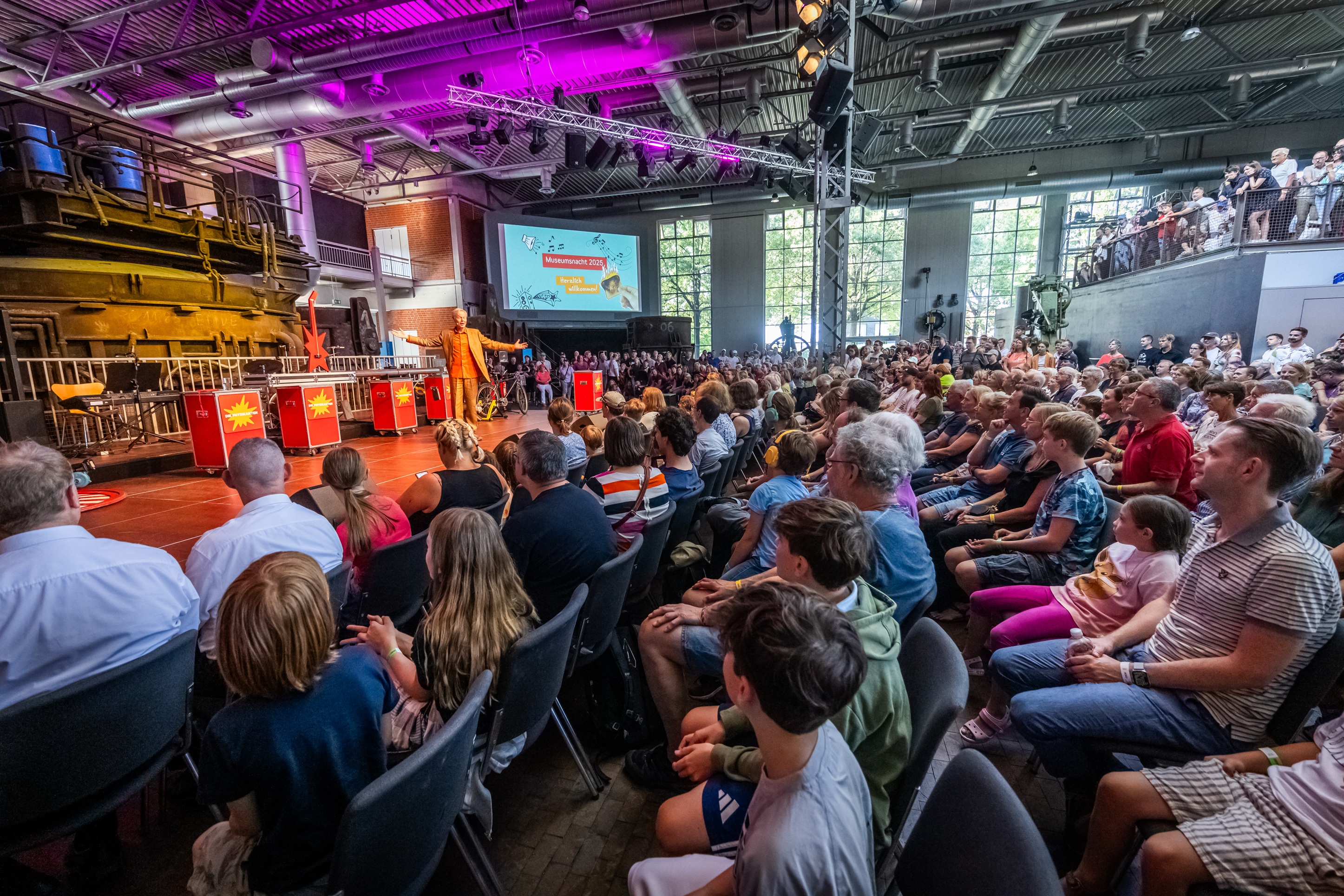 Die Stahlhalle in der DASA beim Auftritt der Physikanten. Zahlreiche der Bühne zugerichtete Stuhlreihen, die gefüllt sind mit Besucher*innen, die sich den Auftritt anschauen.