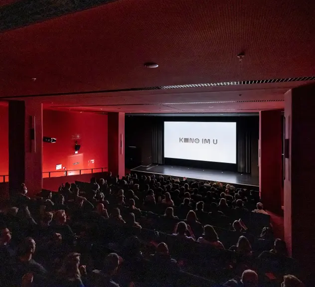 Das Kino im Dortmunder U. Zu sehen ist der dunkle Saal mit roten Wänden, eine weiße Leinwand und viele Kinobesucher*innen auf den Plätzen.