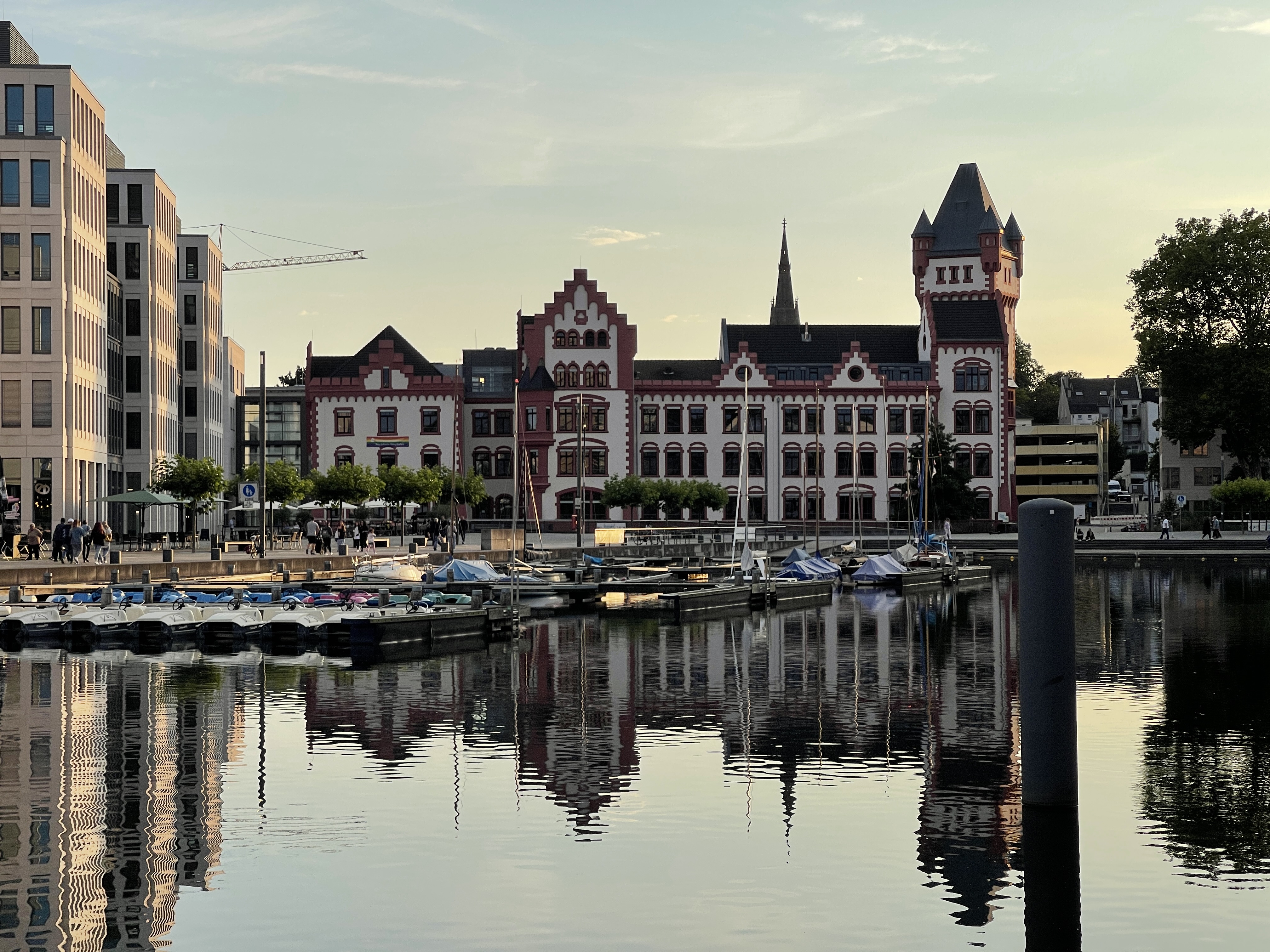 Zu sehen ist die rot-weiße Hörder Burg bei Einbruch des Abends. Sie spiegelt sich auf der Hafen-Seite im Phönix See. Auf dem Wasser befinden sich einige kleine Boote sowie Tretboote.