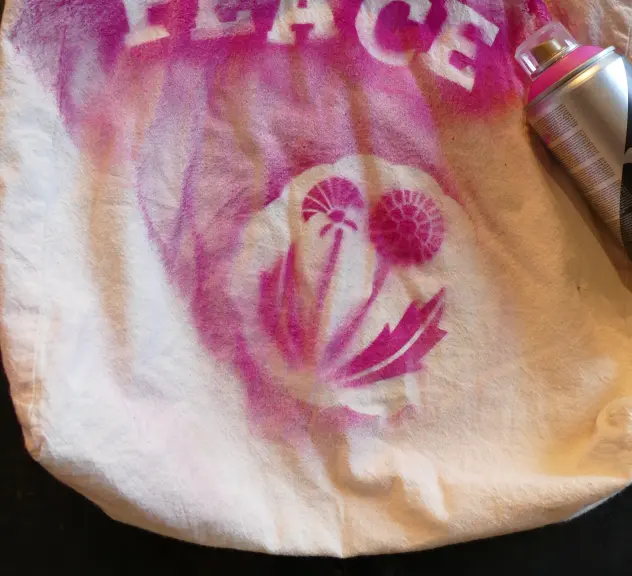 Zu sehen ist ein Jutebeutel, auf welchem mit pinker Farbe das Wort "Peace" aufgesprayt wurde sowie zwei pinke Blumen darunter.