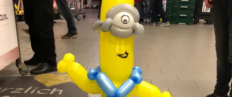 Zu sehen ist eine längliche Minion-Ballonfigur auf einem grünen Skateboard.