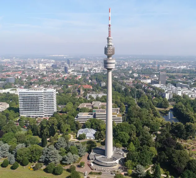 Zu sehen ist der Florianturm und ein Teil des Westfalenparks von oben. Im Hintergrund sieht man viele Gebäude der Stadt, man hat einen weiten Blick.