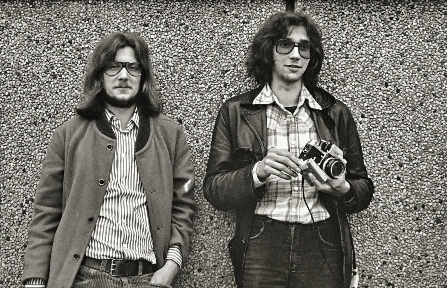 Schwarz-weiß Foto von zwei jungen Männern mit langen Haaren. Einer hält eine Kamera in der Hand.