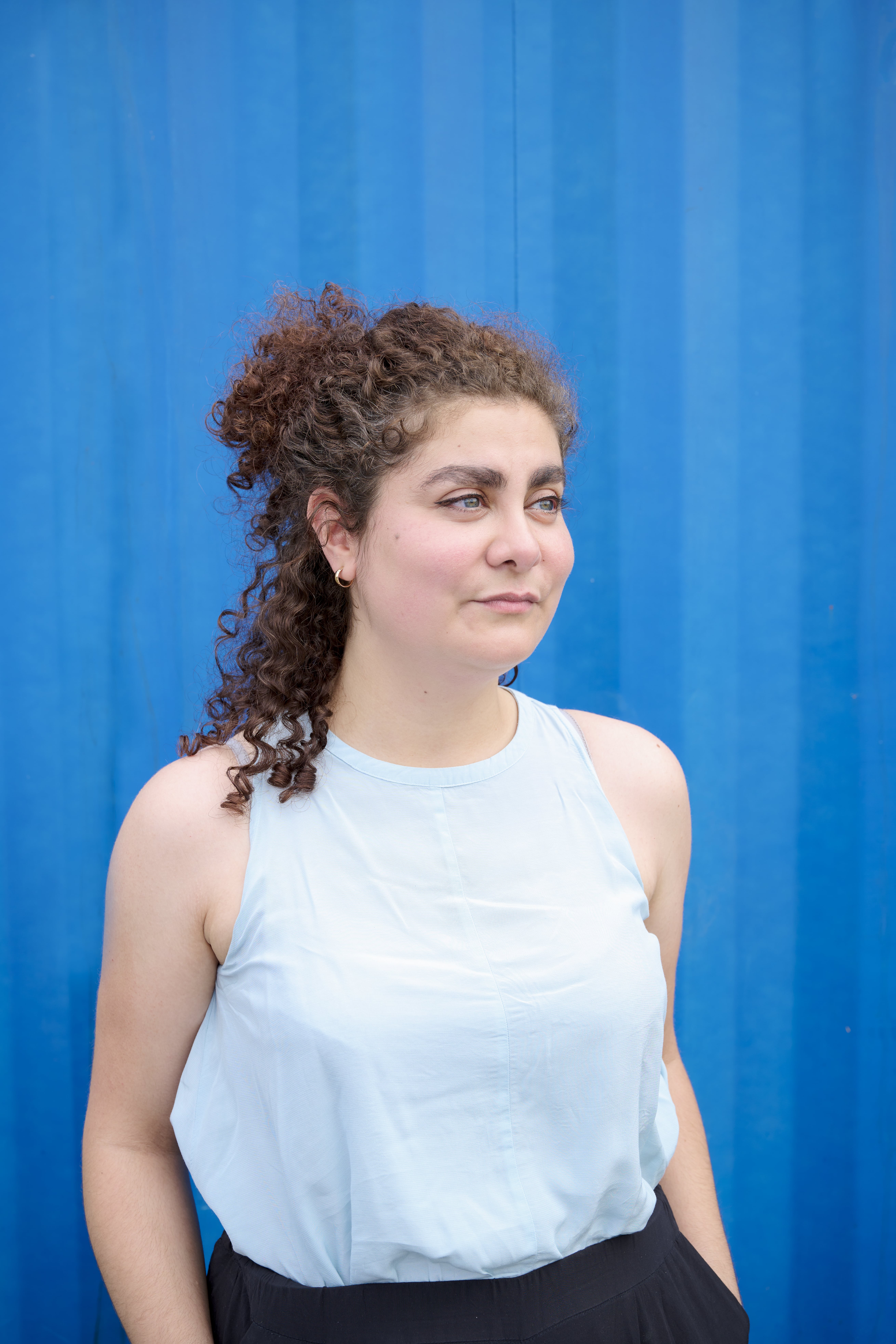 Eine Frau mit dunklen lockigen Haaren blickt zur Seite und lächelt leicht. 